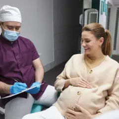 Dentista con mascherina parla con una donna incinta sorridente, discutendo della pulizia dei denti in gravidanza.