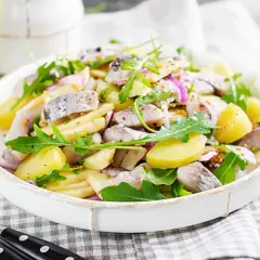 Salade de pommes de terre et hareng à l'huile, garnie de roquette et d'oignons rouges. Une recette simple et savoureuse.
