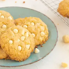Saftige white chocolate macadamia cookies auf einem türkisfarbenen Teller, daneben Macadamianüsse und Schokostückchen.