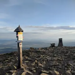 Szczyt Babiej Góry z drogowskazami i kamiennymi obeliskami. Widok na doliny i chmury.