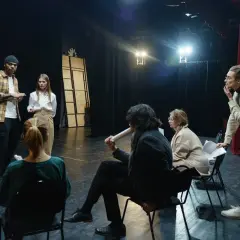 Grupa ludzi na scenie, dyskutująca o sztuce. Zastanawiają się, ile zarabia reżyser w Polsce, analizując scenariusz.
