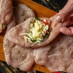 Przygotowanie soczystych roladki z kurczaka z piekarnika. Na surowym mięsie widać ser, pomidora i zioła.
