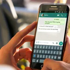 Dłonie trzymają smartfon z otwartym WhatsAppem. Widoczna jest rozmowa i klawiatura, co może pomóc w nauce jak zainstalować WhatsApp.