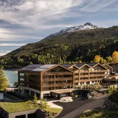 Das Gerstl Family Retreat, un hotel moderno con pannelli solari, si affaccia su un lago alpino e montagne boscose.