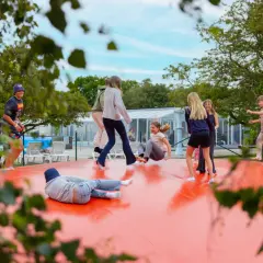 Barn hoppar på en stor orange studsmatta vid first camp råå vallar-helsingborg. Solen skiner och det är en härlig sommardag.