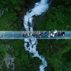 Un gruppo di persone ammira la cascata nel **Val di Rabbi** da un ponte sospeso.