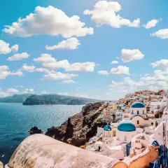 Santorini, Grecja. Białe domy z niebieskimi kopułami kościołów na zboczu góry, morze i chmury. Zastanawiasz się, ile się leci do Grecji?