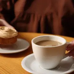 Kawa przed snem z ciastkiem. Dłonie trzymają filiżankę kawy i słodki deser na drewnianym stole.