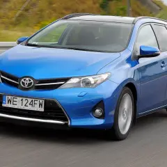 Niebieski Toyota Auris 1.4 D4D w wersji kombi pędzi po drodze, ukazując swoje dynamiczne linie.