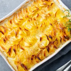 Złociste, zapiekane ziemniaki gratin w białym naczyniu, ozdobione gałązką rozmarynu. Idealne na rodzinny obiad.