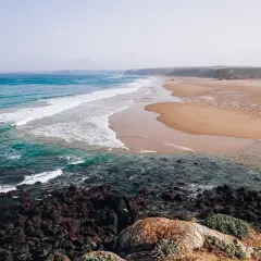 Piękne plaże i turkusowe morze, idealne na algarve wakacje. Surferzy łapią fale, a skały tworzą malowniczy brzeg.