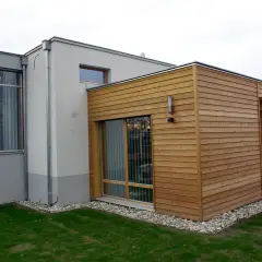 Moderner Anbau an altes Haus: Ein Teil des Hauses ist mit Holz verkleidet, der andere Teil verputzt. Große Fensterfronten und ein Wintergarten.