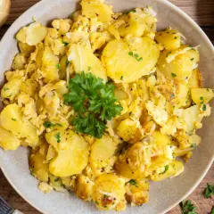 Herzhafte bratkartoffeln mit ei, garniert mit Petersilie. Dazu rohe Kartoffeln und Zwiebeln.