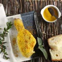 Fusi di pollo al forno dorati e croccanti, serviti con pane fresco, salsa gialla e rametti verdi.