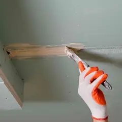 Ręka w rękawicy nakłada masę szpachlową na połączenie płyt gipsowo-kartonowych, przygotowując je do dalszych prac.