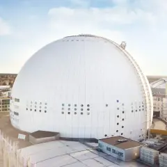 En solig dag vid Globen, Stockholm. Den ikoniska sfäriska arenan dominerar landskapet, omgiven av moderna byggnader och en klarblå himmel.
