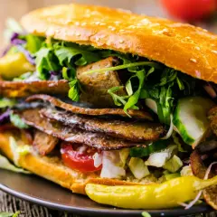 Apetyczny kebab w bułce z mięsem, warzywami i sosem na drewnianym tle.