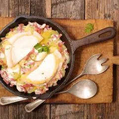Plat de pommes de terre gratinées avec lardons et fromage fondant, servi dans une poêle en fonte. Un plat avec charcuterie réconfortant.