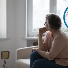 Starsza kobieta siedzi na kanapie, zamyślona. Obok niej w kółku polskie banknoty 500 zł.