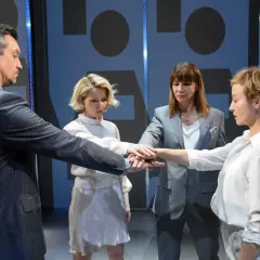 Cztery osoby łączą dłonie w geście jedności. To scena z nienasyceni spektakl, gdzie wspólnie budują coś ważnego.