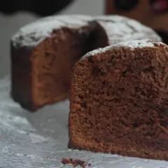 Un trozo de el mejor bizcocho de chocolate del mundo, espolvoreado con azúcar glas, sobre una bandeja de cristal.