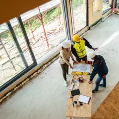 Architekci omawiają projekt, ustalając, ile kosztuje wybudowanie garażu. Na stole plany, narzędzia i próbki materiałów.