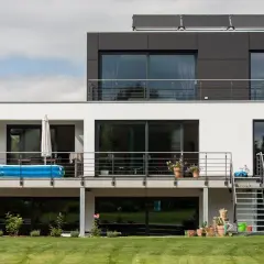Moderne Hausumbau-Ideen: Vorher-Nachher-Vergleich eines weißen Hauses mit dunklem Anbau, Balkon und Pool.