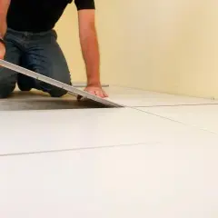 Hombre colocando baldosas blancas, un paso clave para como poner suelo porcelanico.