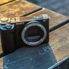 Czarny aparat Sony ZV-E10 II bez obiektywu leży na drewnianym stole, oświetlony ciepłym, zachodzącym słońcem.