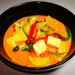 Ein dampfendes rotes Curry mit Tofuwürfeln, grünen Tomaten und scharfen Chilischoten. Dieses rote Curry ist scharf und verlockend.