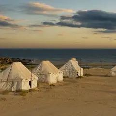 Namioty na piaszczystej plaży nad oceanem o zachodzie słońca.
