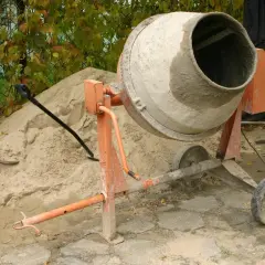Betoniarka czeka na materiały, by pokazać, jak zrobić beton. Obok piasek, łopata i kapelusz.