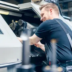 Operator CNC w kombinezonie pracuje przy maszynie, regulując jej elementy.