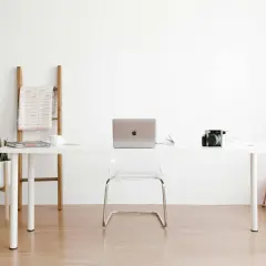 Ein moderner Arbeitsplatz mit einem weißen Schreibtisch, Laptop, Kamera und einer Pflanze. Perfekt für alle, die einen **tisch selber bauen** möchten.