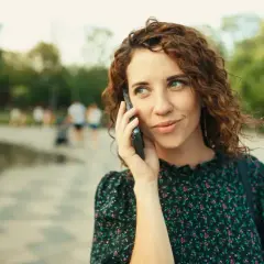 Kobieta z kręconymi włosami rozmawia przez telefon, zastanawiając się, jak odsłuchać pocztę głosową plus.