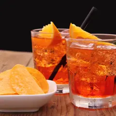 Dwa orzeźwiające drinki z pomarańczą i słone chipsy na drewnianym stole, idealne na aperitif.