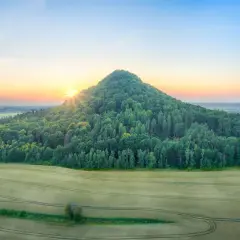 Wzgórze porośnięte lasem, przypominające wygasłe wulkany w Polsce, oświetlone wschodzącym słońcem.
