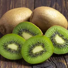 Kiwi na refluks. Dwa całe owoce kiwi i cztery przekrojone na pół, ukazujące zielony miąższ z czarnymi pestkami, leżą na drewnianym blacie.