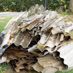 Ein Haufen alter Wellplatten, einst aus faserzement gefertigt, liegt auf einer Wiese. Moos und Schmutz bedecken die verwitterten Oberflächen.