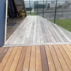 Terrasse en bois avec une partie grise, signe qu'il faut enlever le saturateur bois. Une table et une chaise jaunes sont visibles.