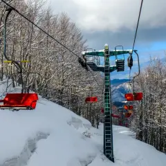 Seggiovia rossa su piste innevate ad Abetone, l'altitudine offre panorami mozzafiato tra alberi spogli coperti di neve.