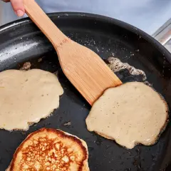 Buttermilch pancakes braten in der Pfanne. Ein Holzspatel wendet einen goldbraunen Pancake.
