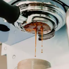 Frisch gebrühter Espresso tropft aus der Siebträgermaschine. Der goldbraune Strahl deutet auf ein perfektes espresso ratio hin.