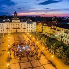 Wieczorny stary rynek płock, z ratuszem i fontanną, oświetlony latarniami, z tłumem ludzi.