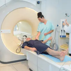 Pacjent leży na łóżku przed aparatem MRI, gdzie pielęgniarka przygotowuje go do badania. To właśnie mri co to za badanie?