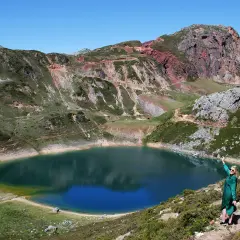 Mujer en la ladera disfruta de las vistas de un lago azul rodeado de montañas, ideal para rutas en Somiedo.
