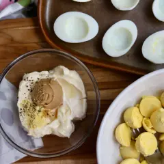 Ingredients for miso egg salad: mayonnaise, miso paste, pepper, and separated egg yolks in a bowl. Halved hard-boiled eggs are on a tray.