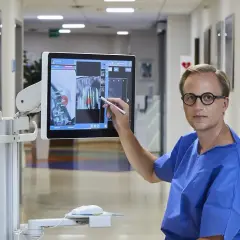 Lekarz w szpitalnym korytarzu analizuje na ekranie wyniki biopsji prostaty, wskazując na niepokojące dane.