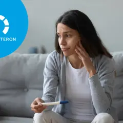 Zmartwiona kobieta trzyma test ciążowy, obok ikona progesteronu.