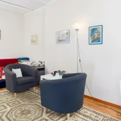 Accogliente studio psicologo in casa, con divano letto, poltrone, tappeto e quadri colorati.